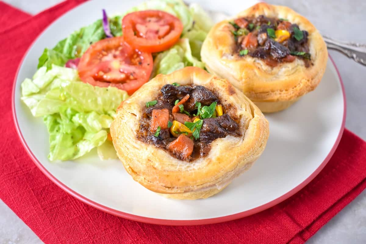 Two mini beef pot pies served on a white plate with a side salad.