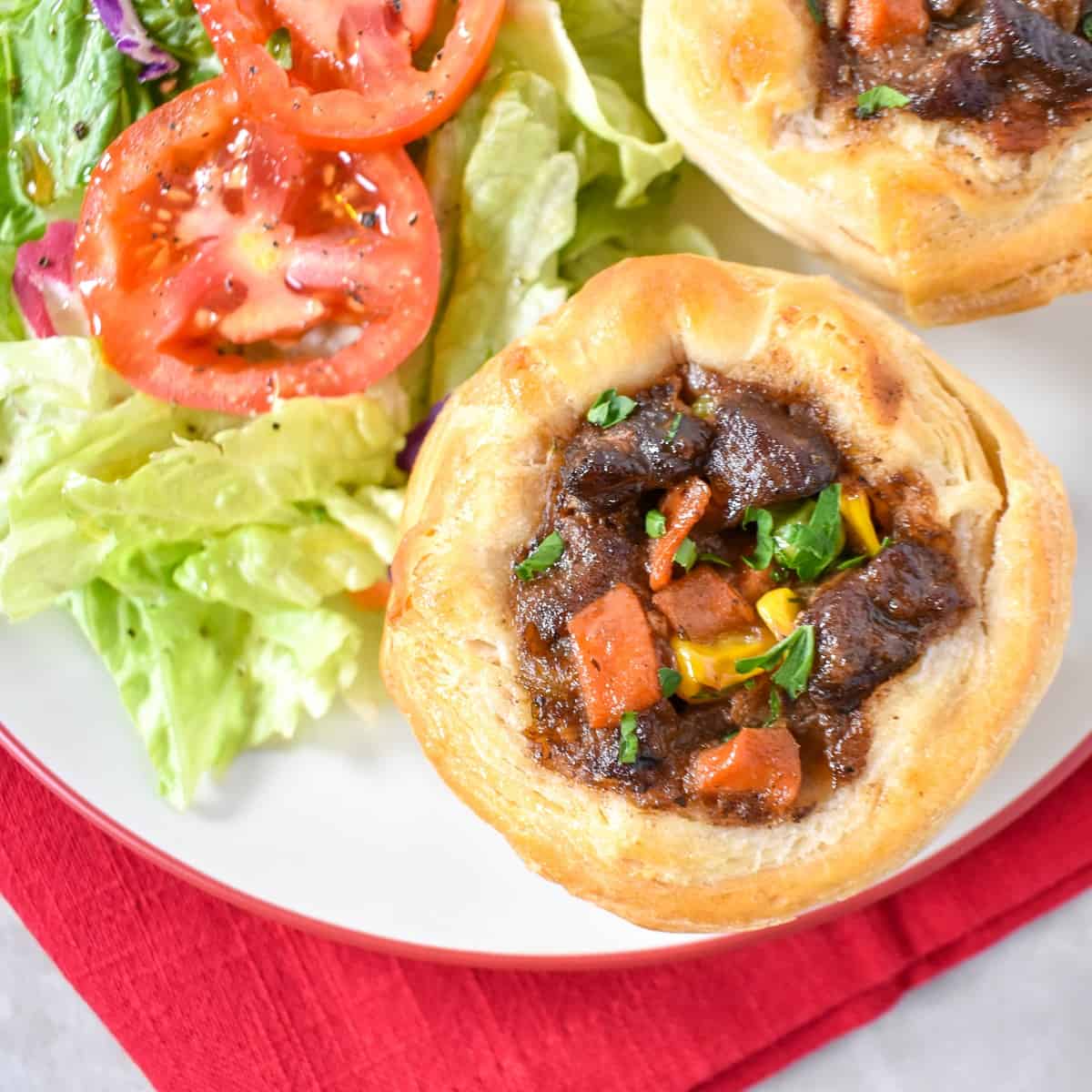 Two mini beef pot pies served on a white plate with a side salad.