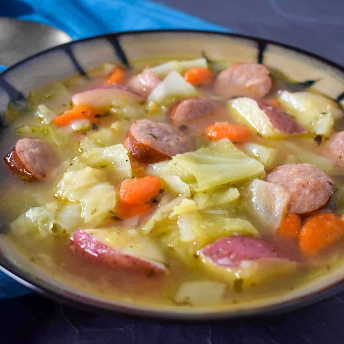 Cabbage sausage soup served in a beige and black bowl.