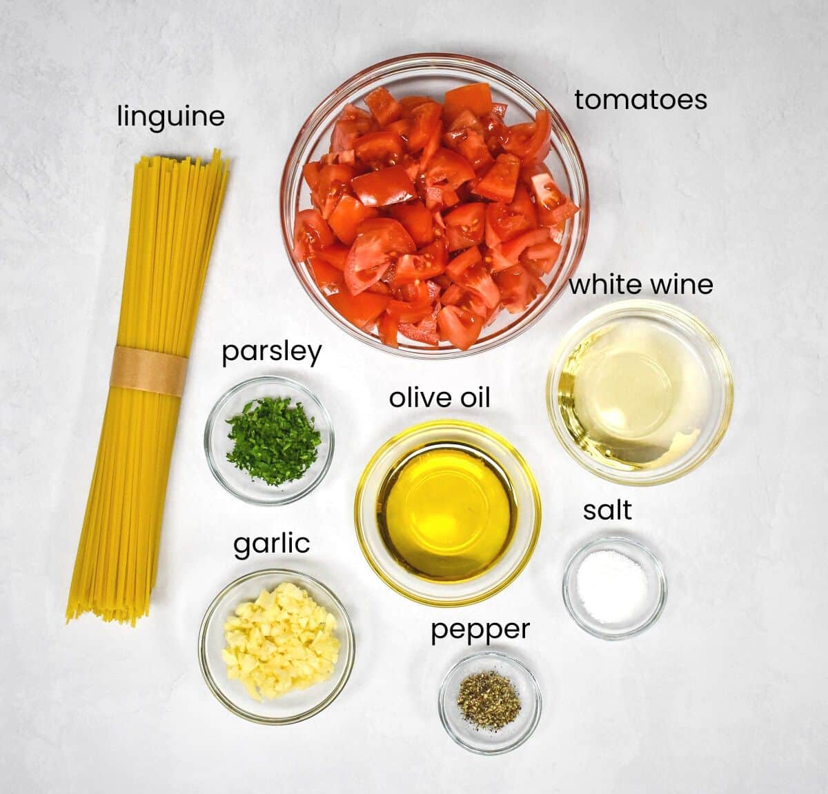 The ingredients for the dish arranged in glass bowls on a white table with each ingredient labeled with small black letters.