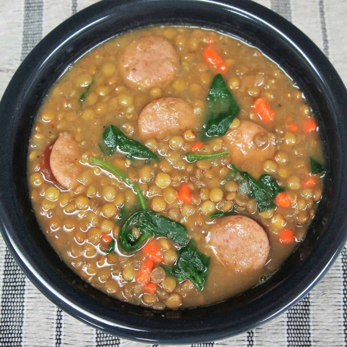 Lentil sausage soup served in a dark gray bowl.