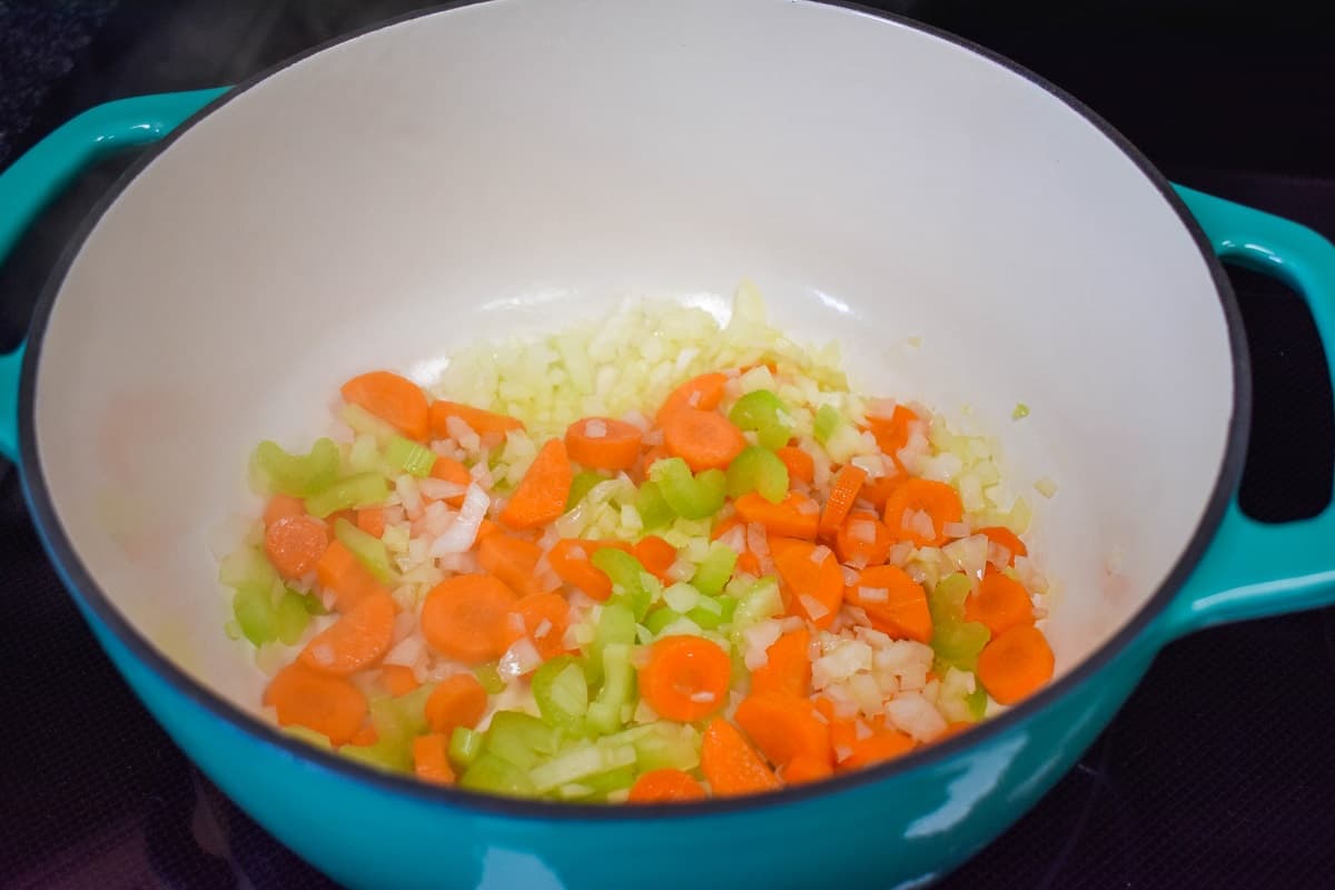 Diced carrots, onions, and celery cooking in a large aqua and white pot.