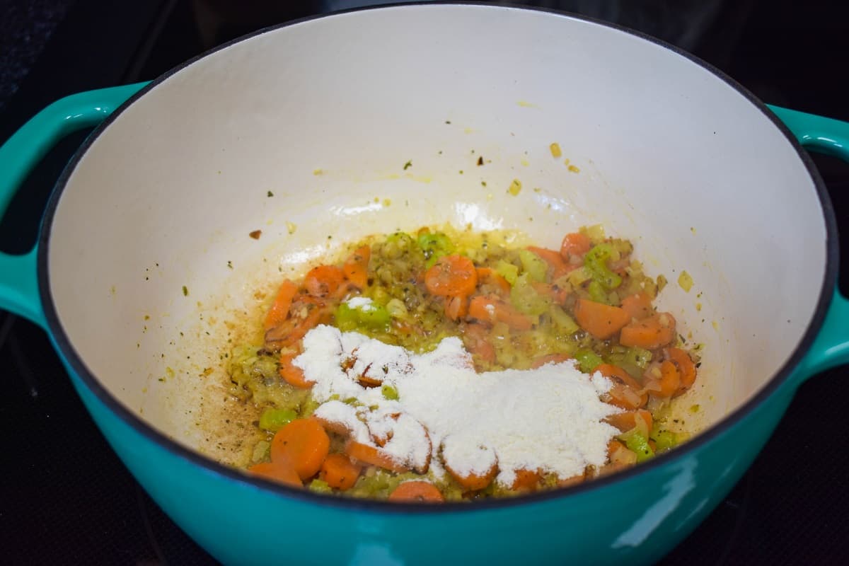 Flour added to the sautéed vegetable mix in a large white and aqua pot.