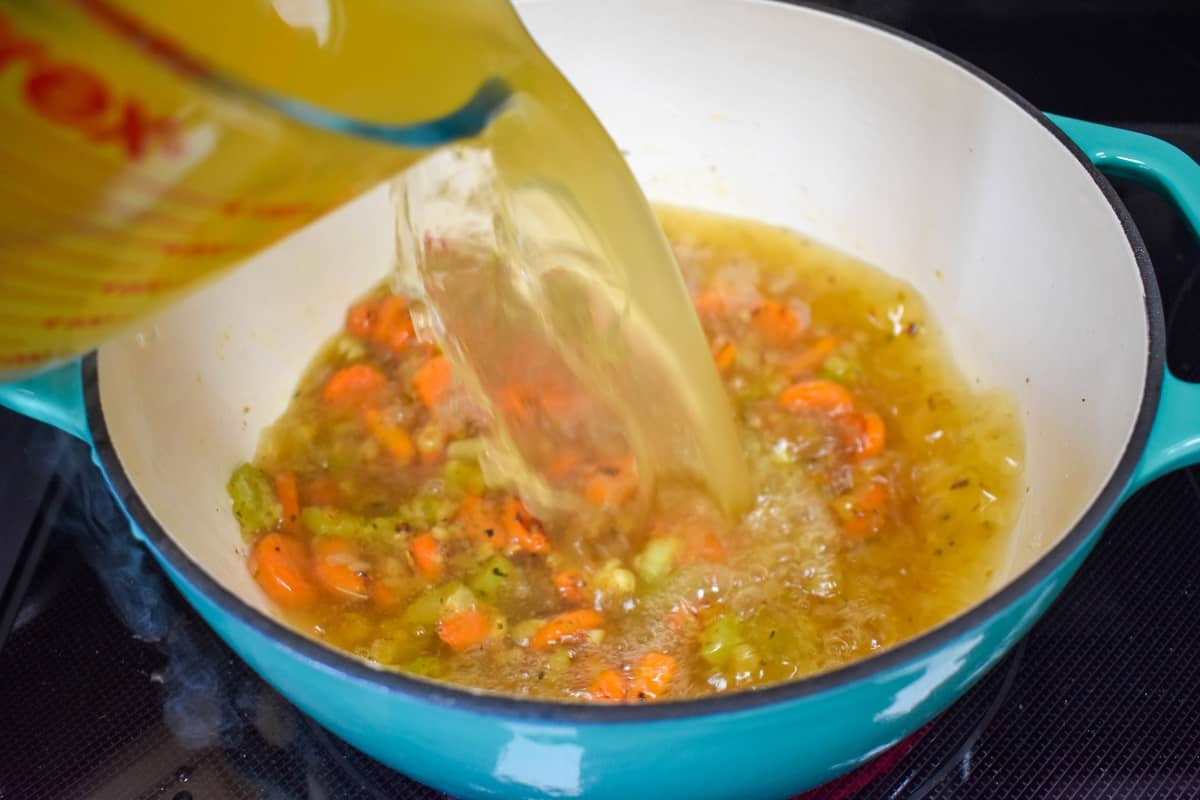 Chicken broth being added with a measuring cup to the vegetables in the pot.
