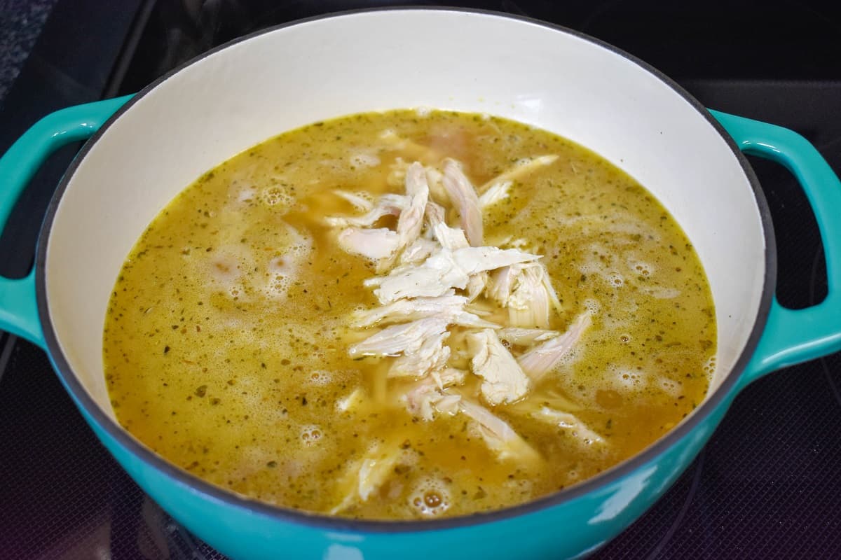 Shredded turkey added to the soup in a large, aqua and white pot.