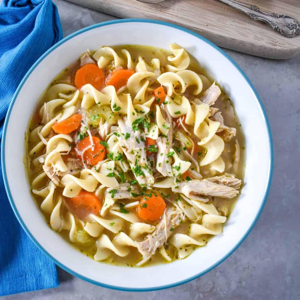 The turkey noodle soup served in a white bowl with a blue linen.