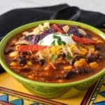 Turkey taco soup served in a green bowl and set on a colorful southwestern style plated with a black napkin and spoon in the background.