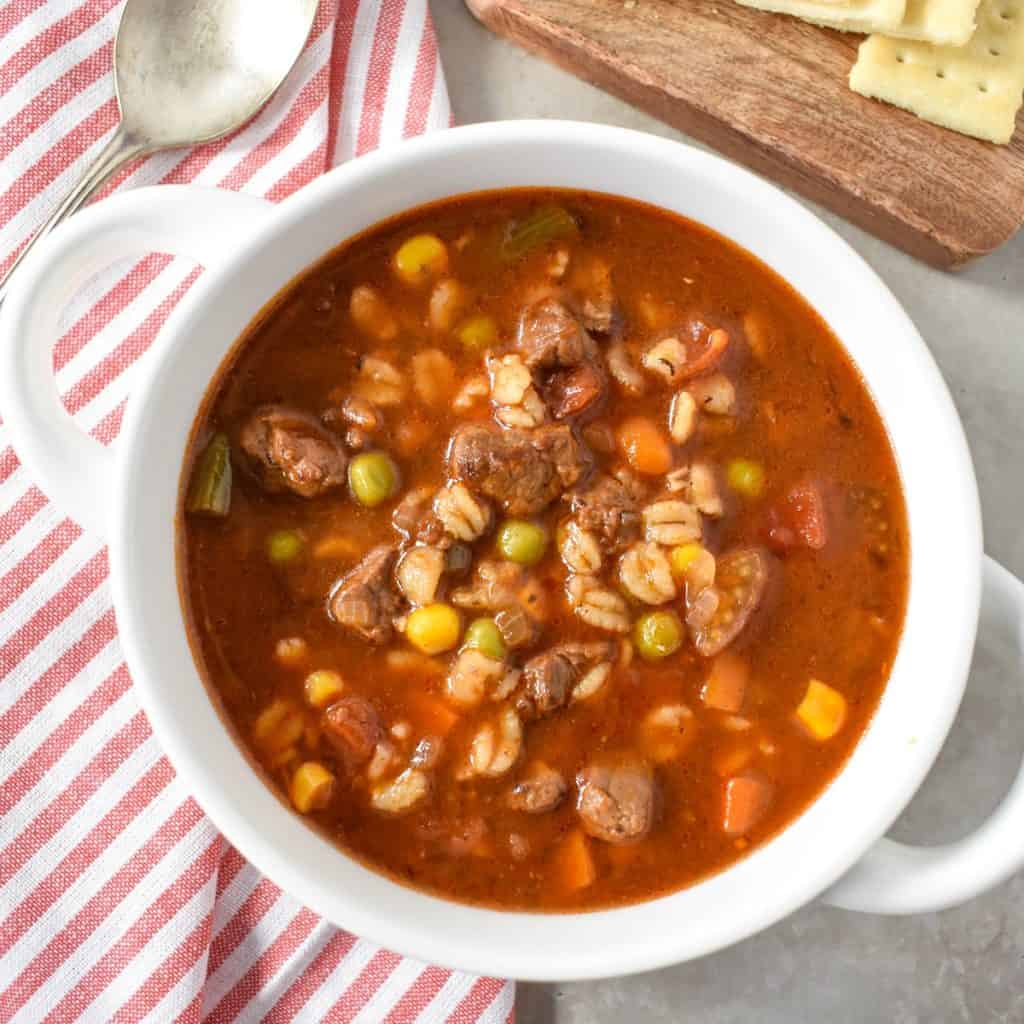 The finished beef barley soup served in a white bowl set on red and white striped linen.