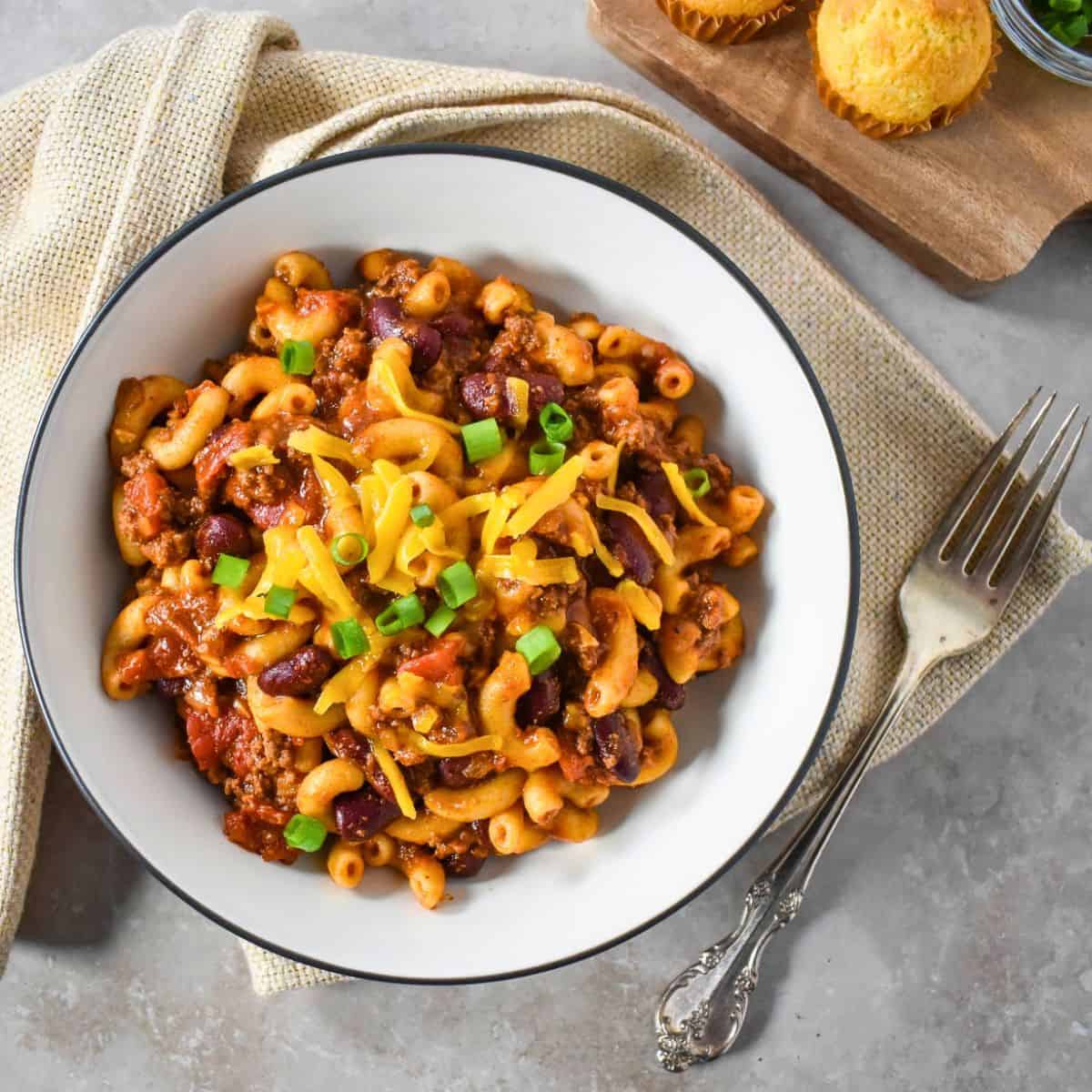 Finished chili mac with ground beef, red beans, and elbow macaroni, topped with shredded cheddar cheese and green onions.
