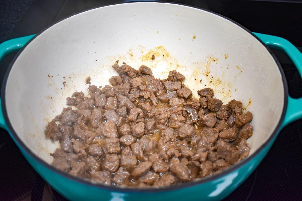 Browned, diced steak browning in a large, teal and white pot.