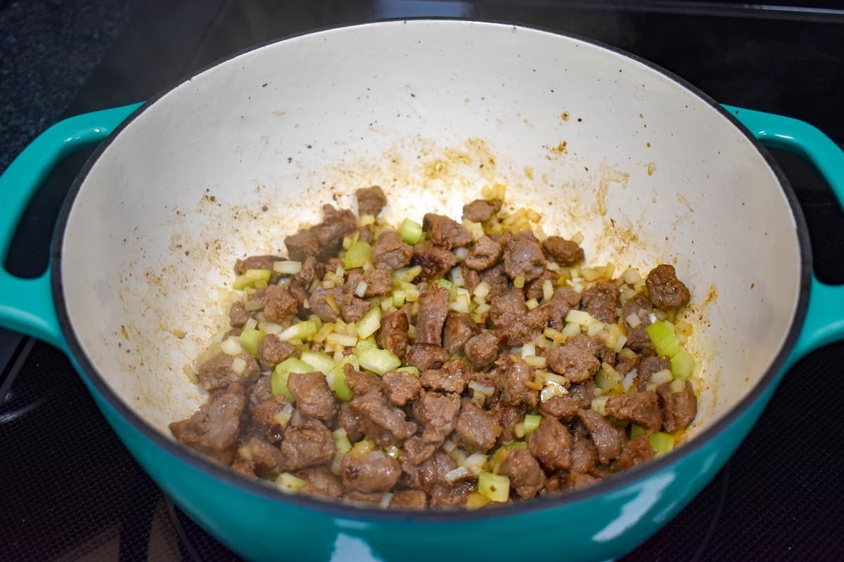 The browned beef with the diced onion and celery cooking in a large, teal and white pot.