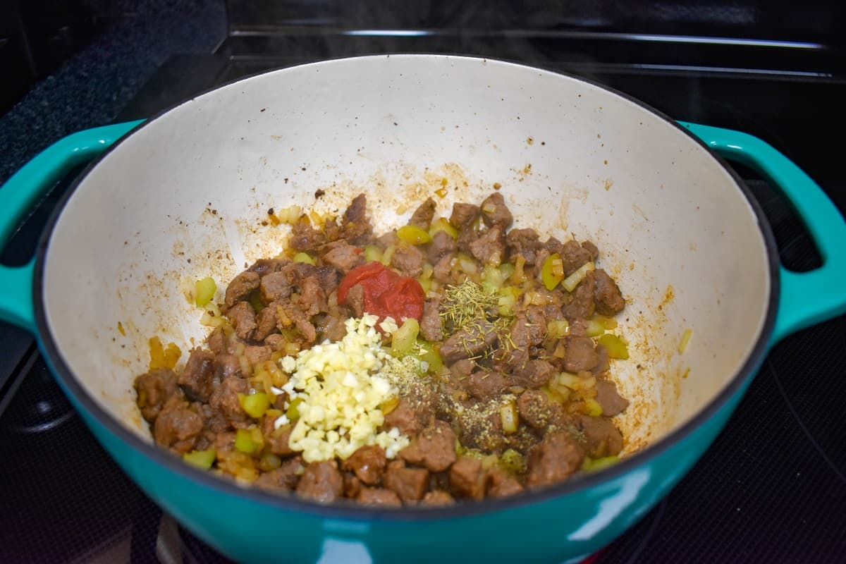 Minced garlic, seasoning, and tomato paste added to the steak and onion mixture.