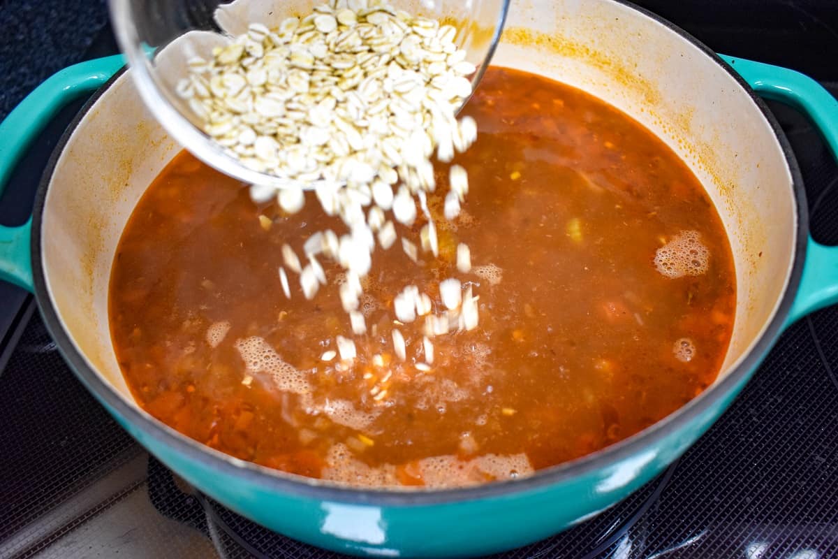 Barley being added to the soup in a large teal and white pot.