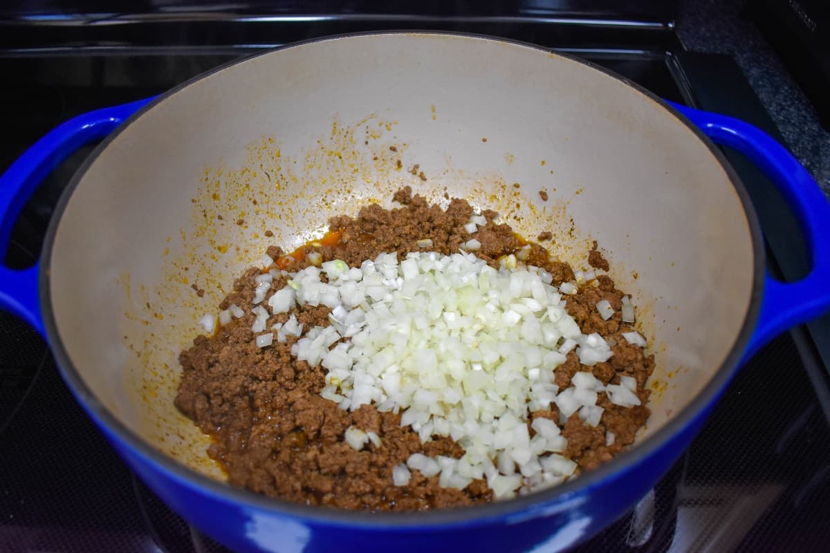 Diced onions added to the browned ground beef in a large blue and white pot.