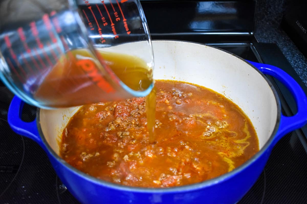 Beef broth being added to the ingredients in the pot.