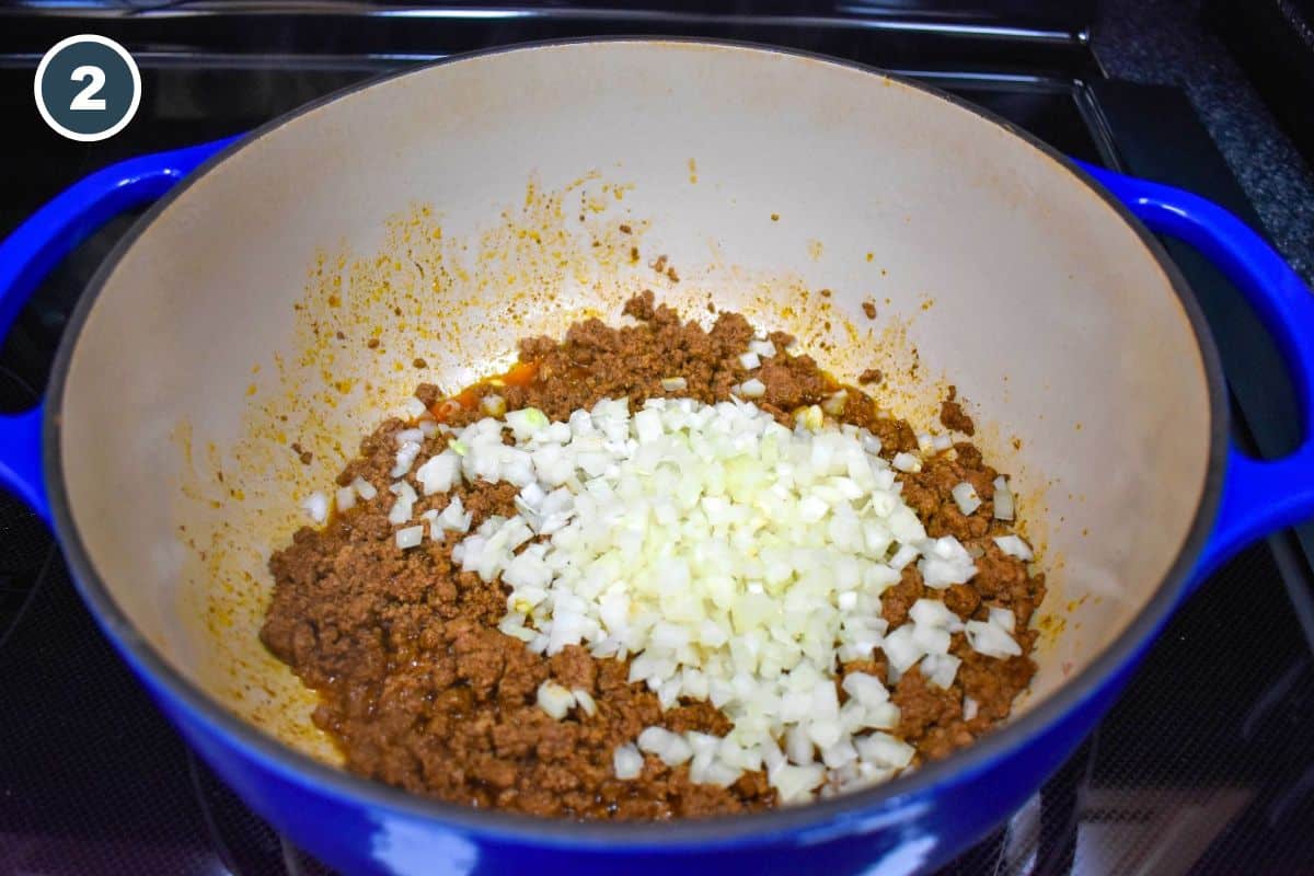 Diced onions added to browned ground beef in a Dutch oven.