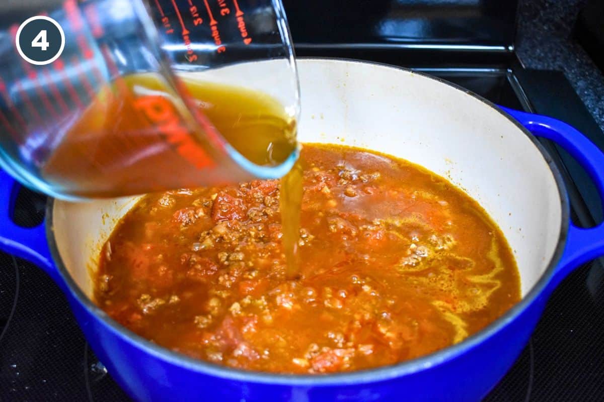 Beef broth being poured into the tomato and ground beef mixture.