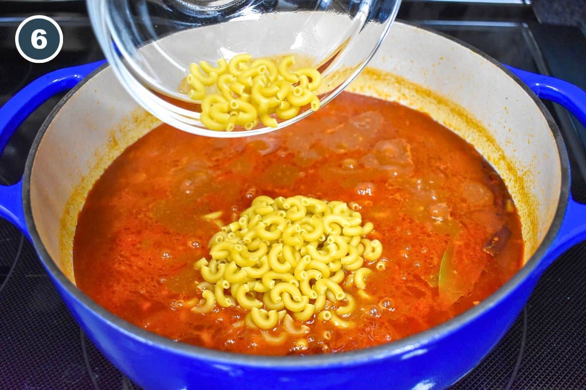 Dry elbow macaroni being added to the simmering chili mixture.