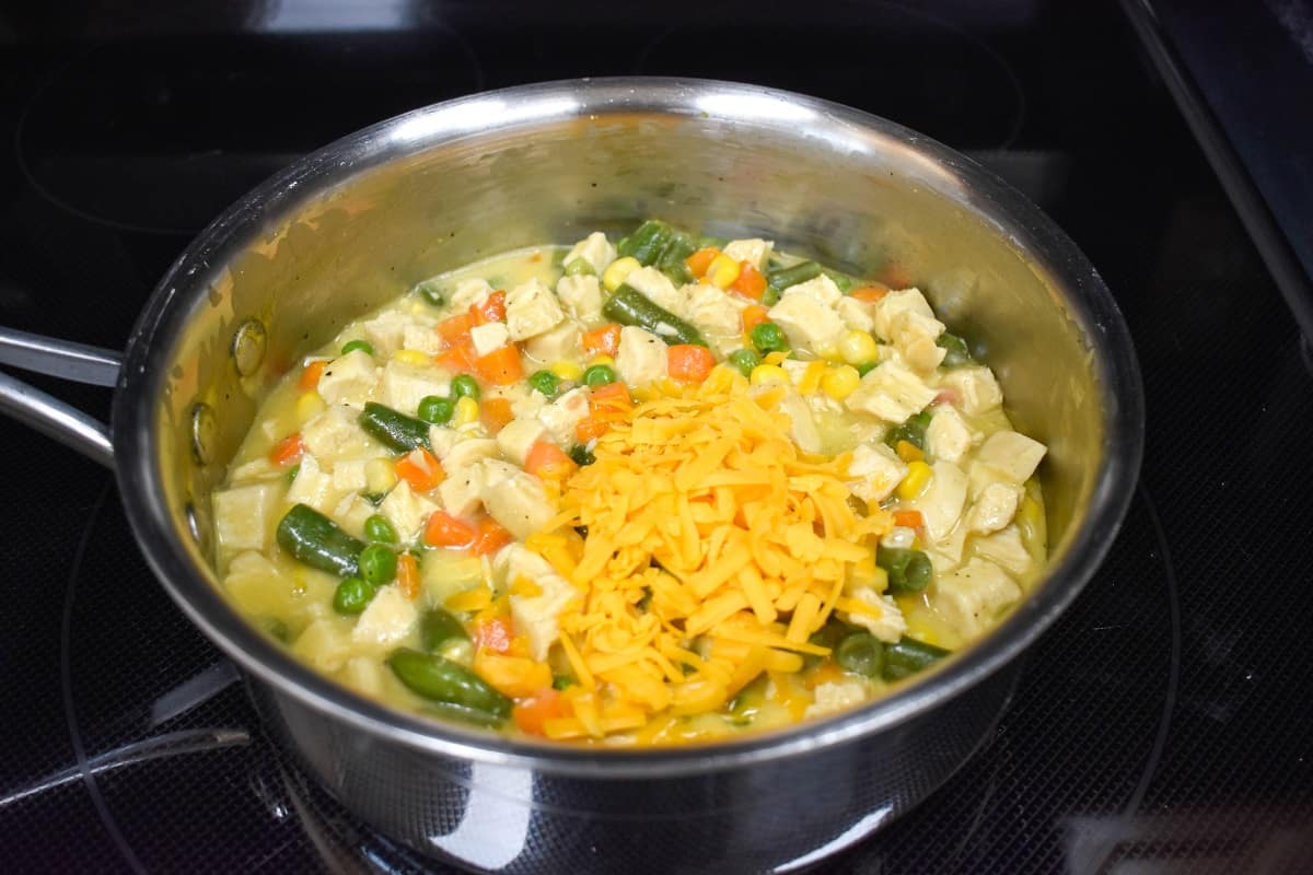 Shredded chicken added to the pot pie filling in a saucepan.