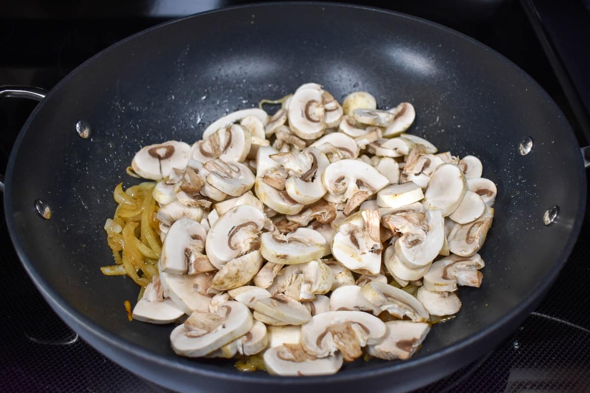 Sliced mushrooms added to the onions in the skillet.