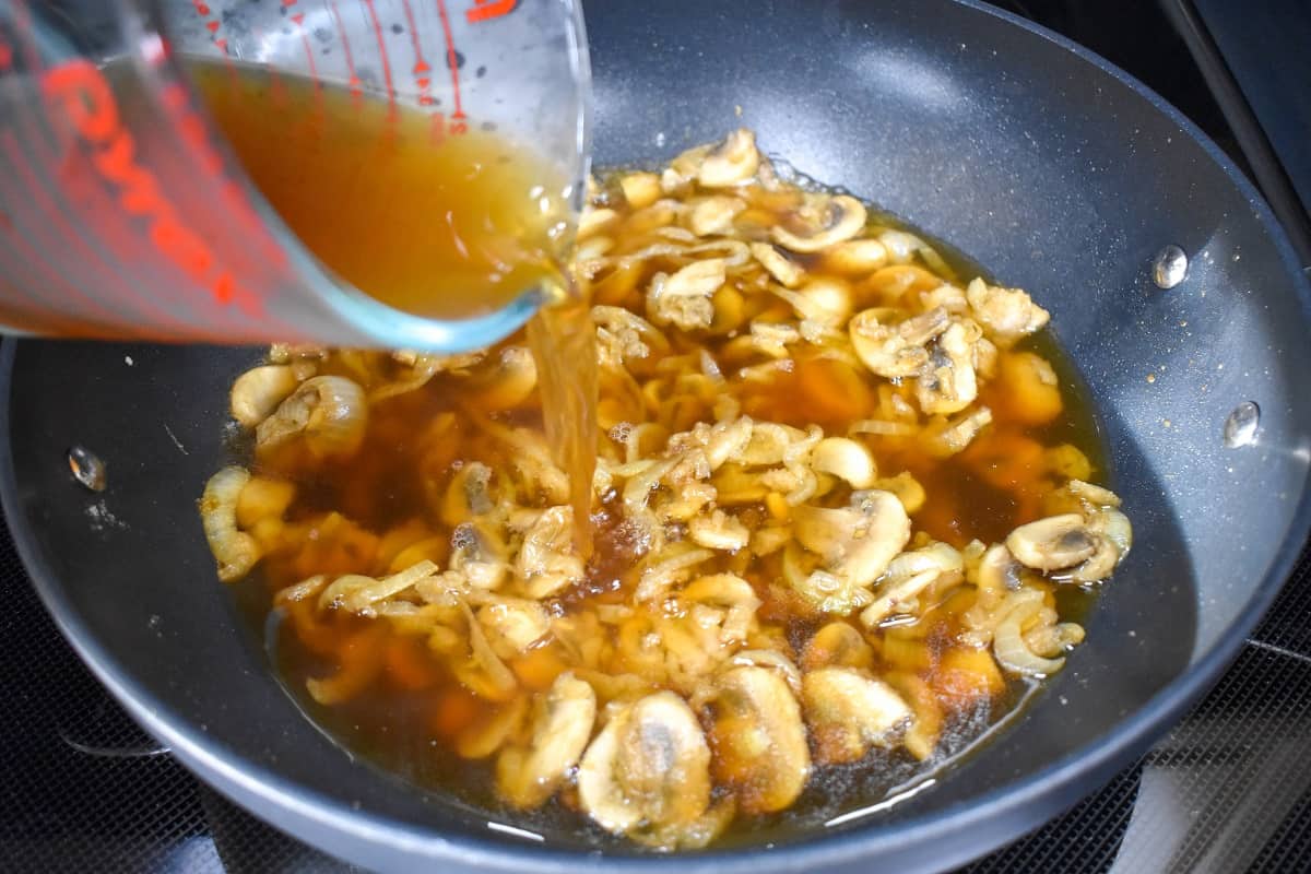 Beef broth being added to the onion mushroom mixture.