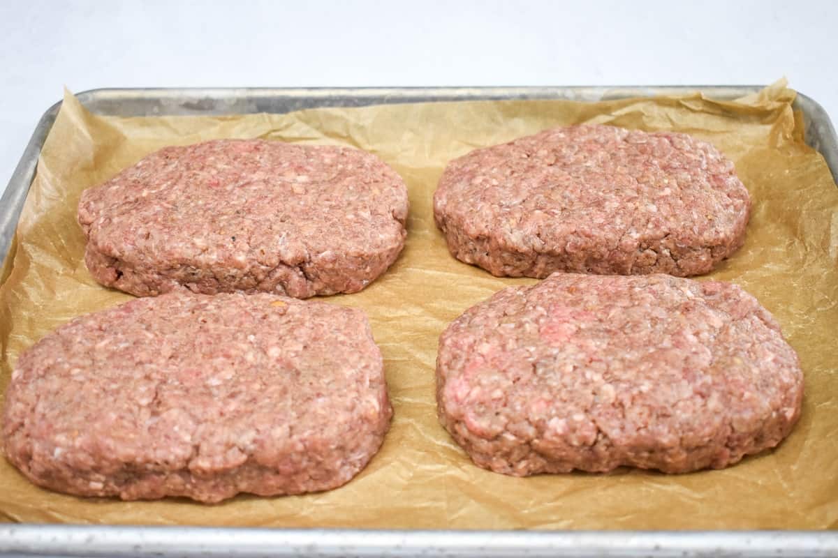 Four patties arranged on parchment paper on a baking sheet.
