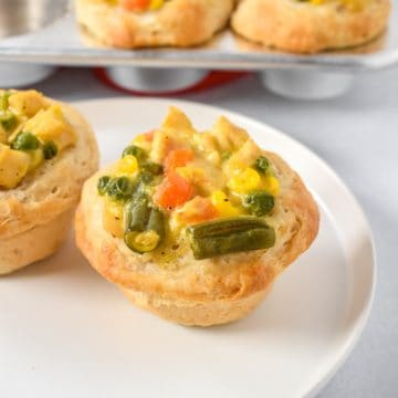 An image of two mini pot pies on a white plate, but only one is in the center the other is half visible along with a little of the muffin pan in the background.