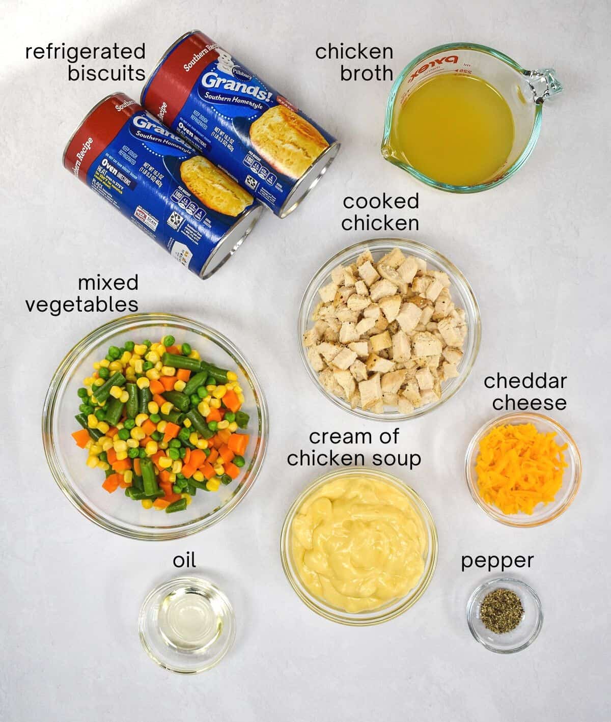 The ingredients for the mini chicken pot pies arranged on a white table with each ingredient labeled with small, black letters.