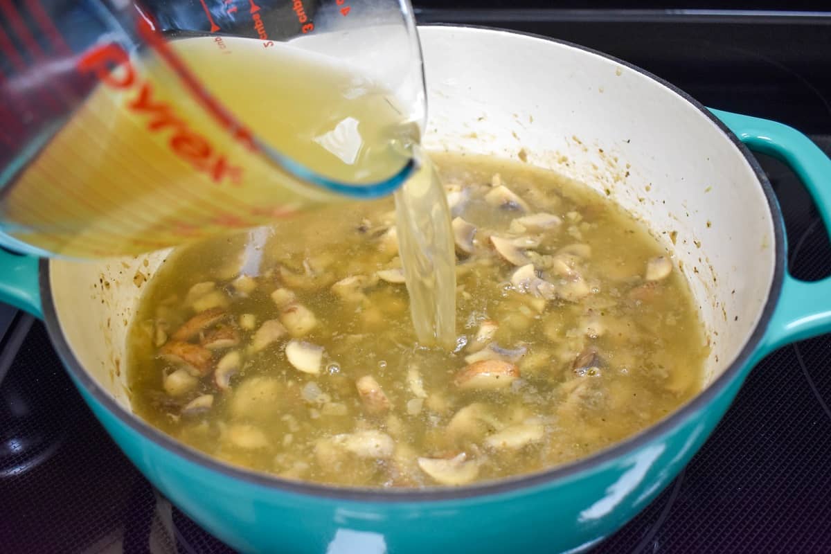Chicken broth being added to the mushroom mixture in an aqua and white pot.