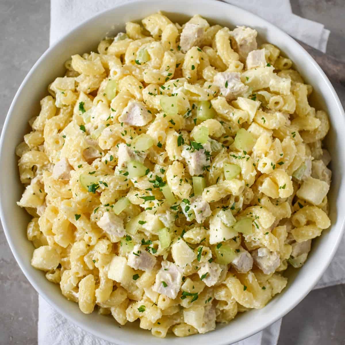 A close up of the chicken macaroni salad garnished with chopped parsley and diced celery served in a white bowl.