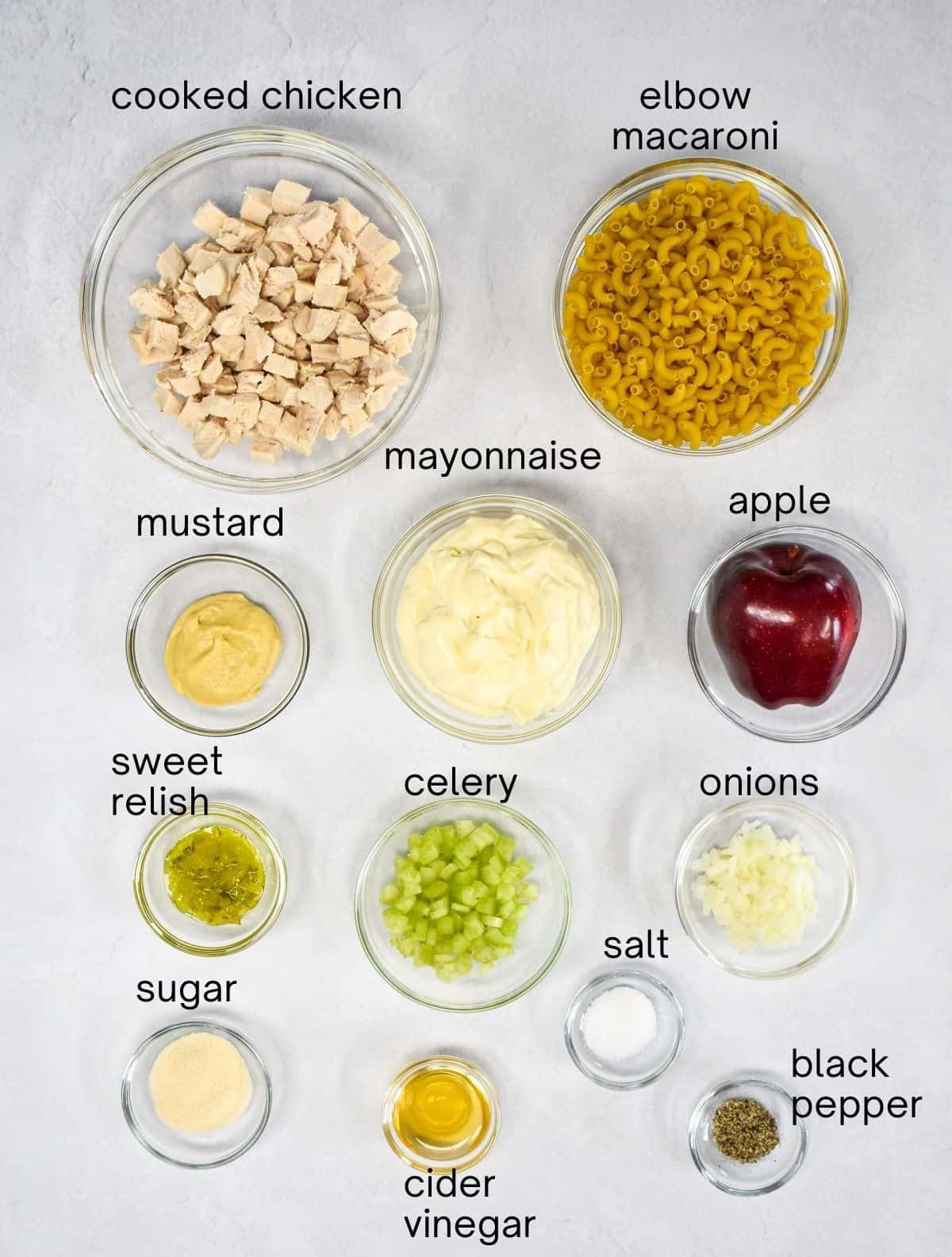 The ingredients for the side dish arranged in glass bowls on a white table. Each ingredient is labeled with small, black letters.