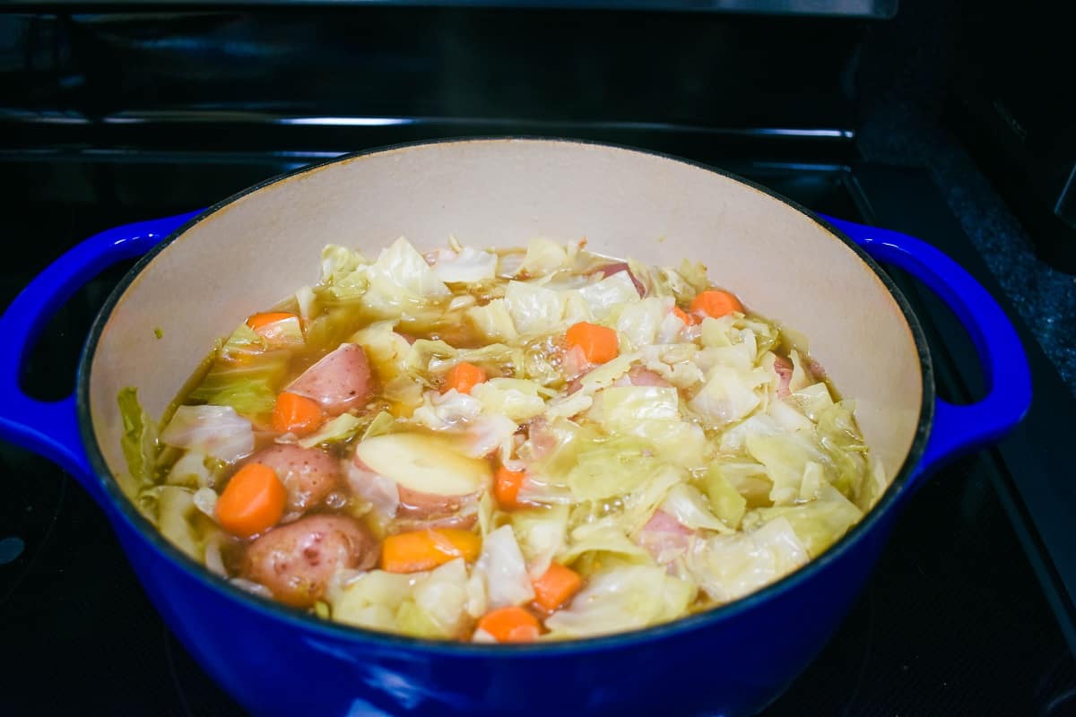 Cabbage, carrots, and potatoes added in broth in a large, blue pot partially cooked.