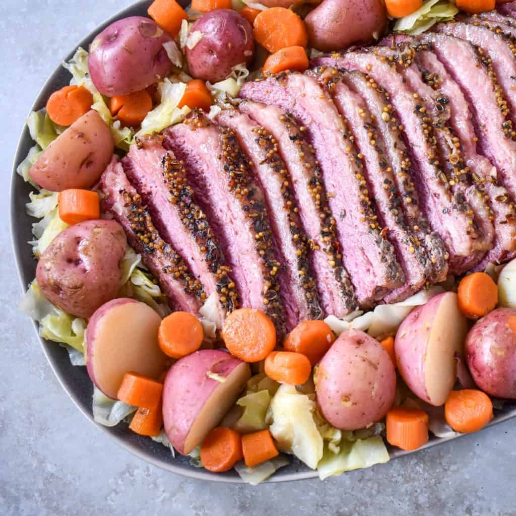 Corned beef, cabbage, potatoes, and carrots arranged on a large platter with the beef sliced into thin pieces.