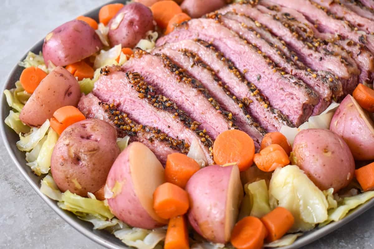 A close-up image of sliced corned beef, cabbage, potatoes, and carrots arranged on a large platter.