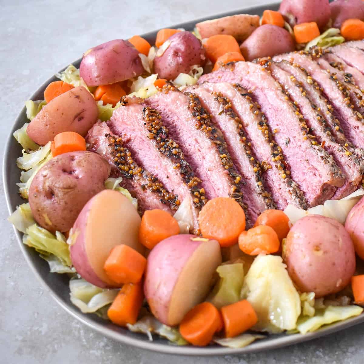 A close-up image of sliced corned beef, cabbage, potatoes, and carrots arranged on a large platter.