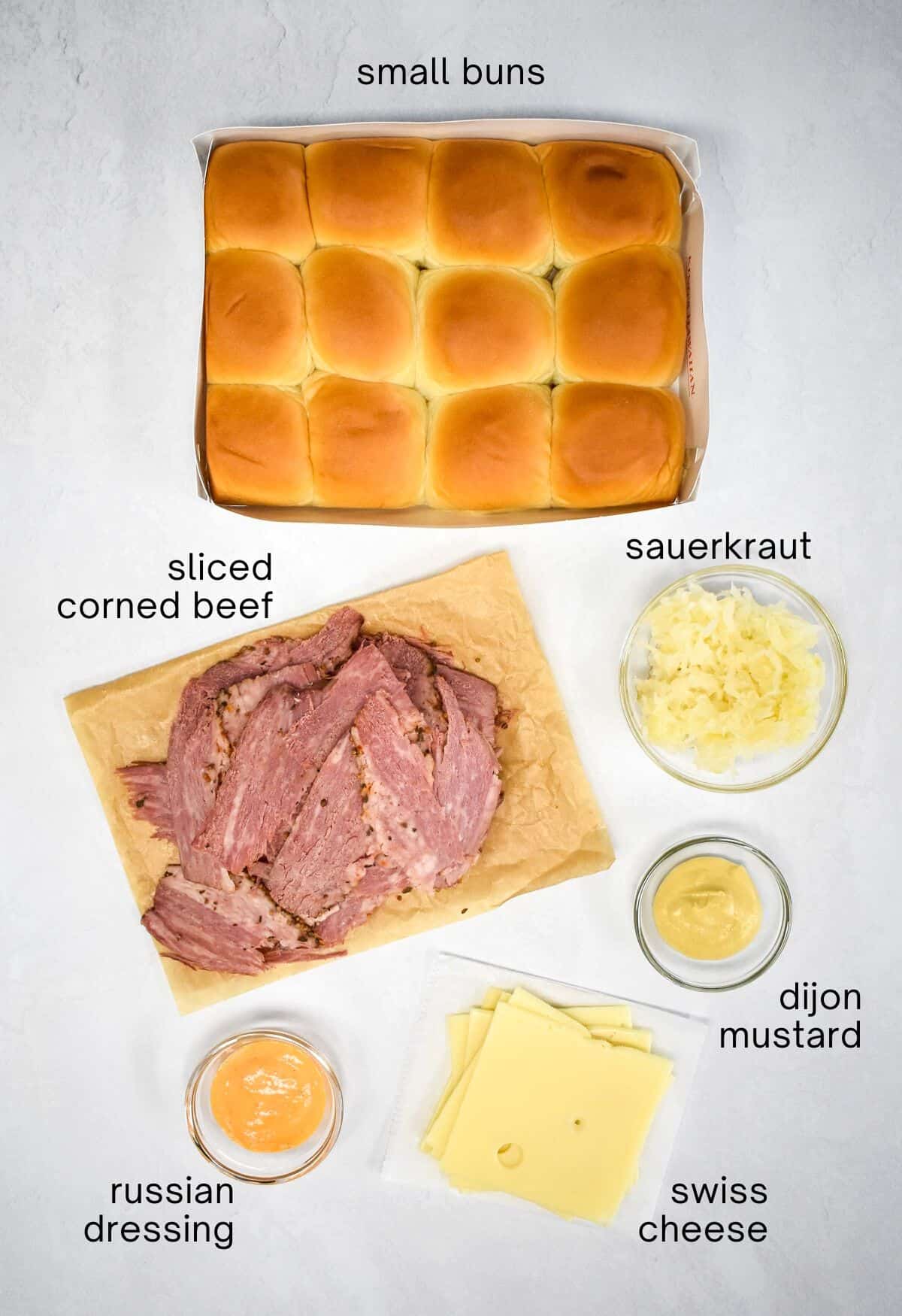 The ingredients for the sandwiches arranged on a white table with each labeled with the name in small, black letters.