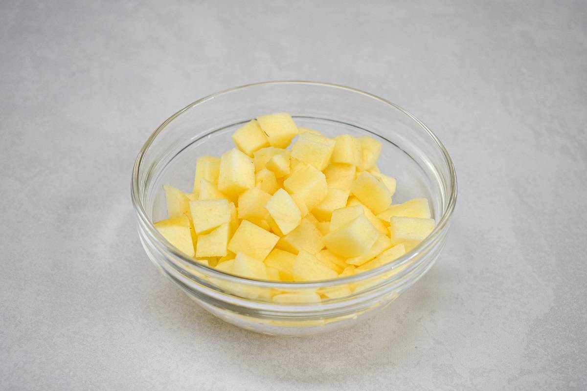Peeled, diced apple in a glass bowl set on a white table.