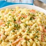 The macaroni salad in a white serving bowl and a teal graphic above it in white letters.