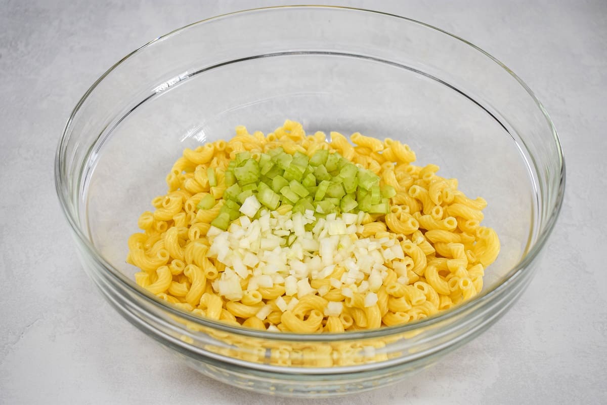 Cooked macaroni, diced onion and celery in a large, glass bowl.