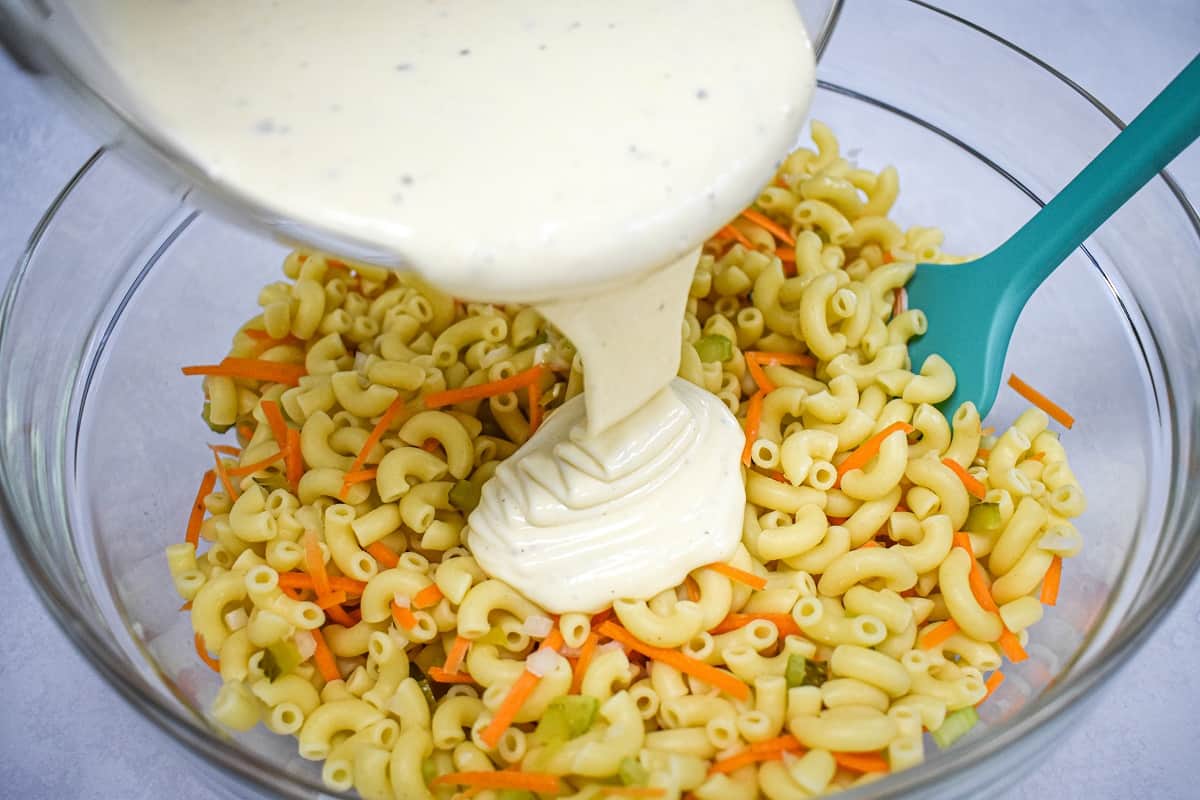 The prepared dressing being added to the macaroni mixture in a large, glass bowl.