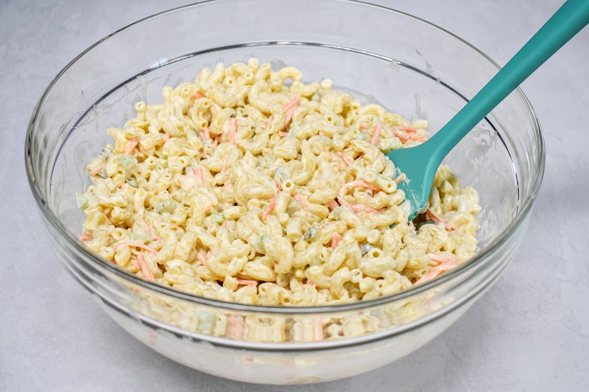 The macaroni tossed with the dressing in a large, glass bowl with a teal silicone spatula.
