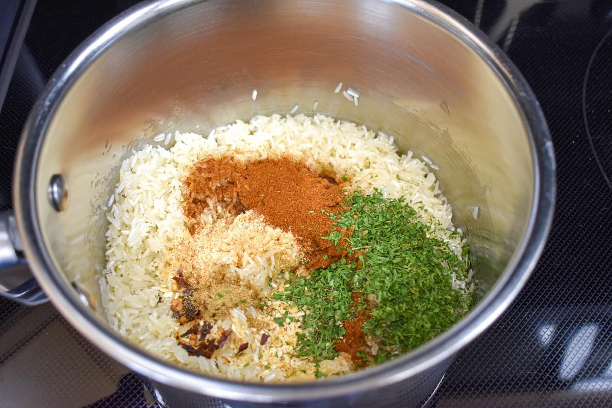 White rice, paprika, dried parsley, garlic powder and other seasoning in a saucepan.