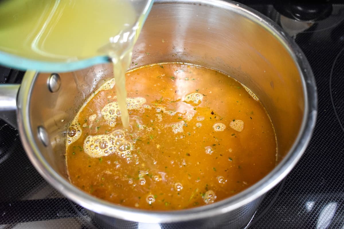 Chicken broth being added to the saucepan with the rice and seasoning.