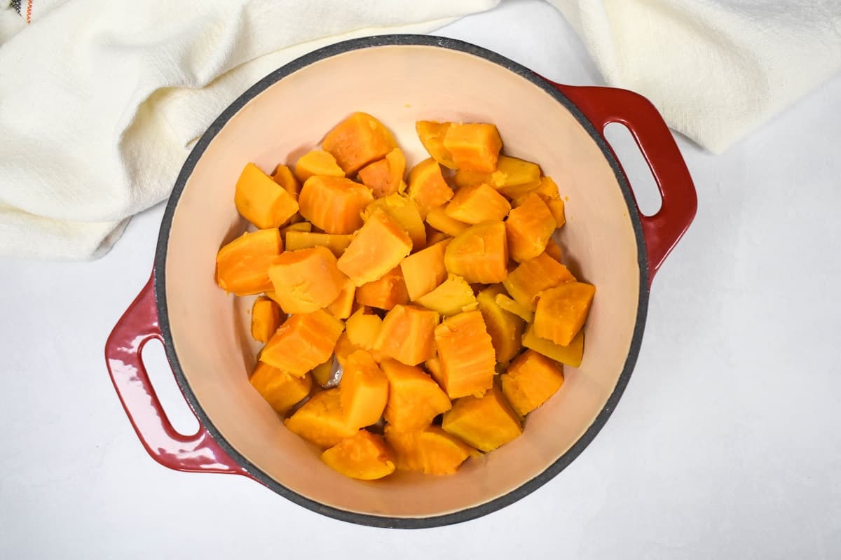 The diced, cooked, and drained sweet potatoes in a red and white pot set on a white table.