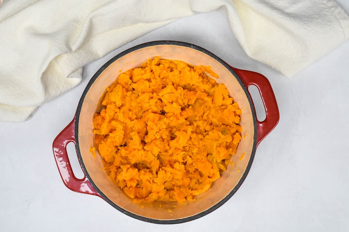 Roughly mashed sweet potatoes in a red and white pot set on a white table.