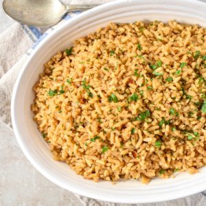 The seasoned rice in a white serving bowl garnished with fresh chopped parsley.