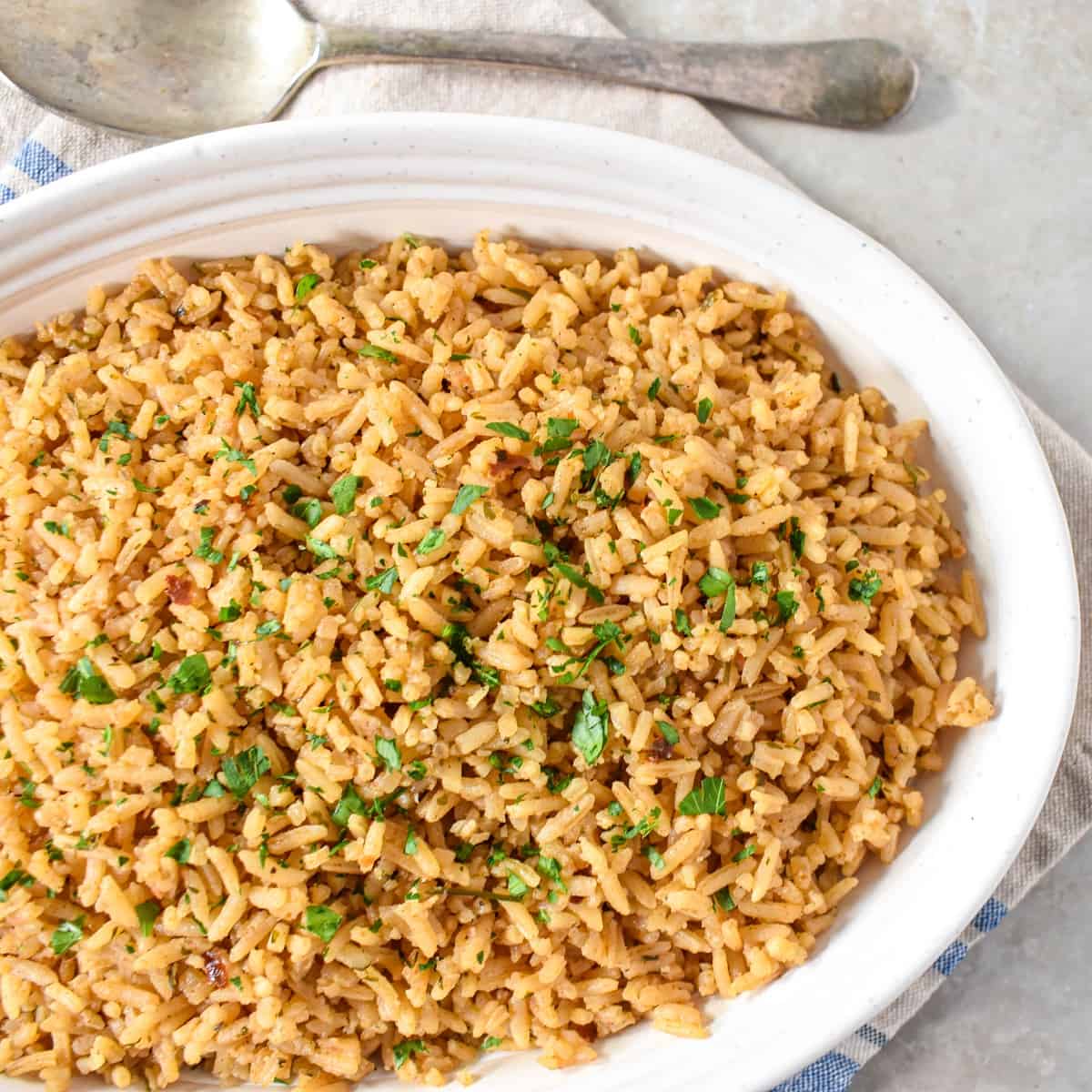 The seasoned rice in a white serving bowl garnished with fresh chopped parsley.