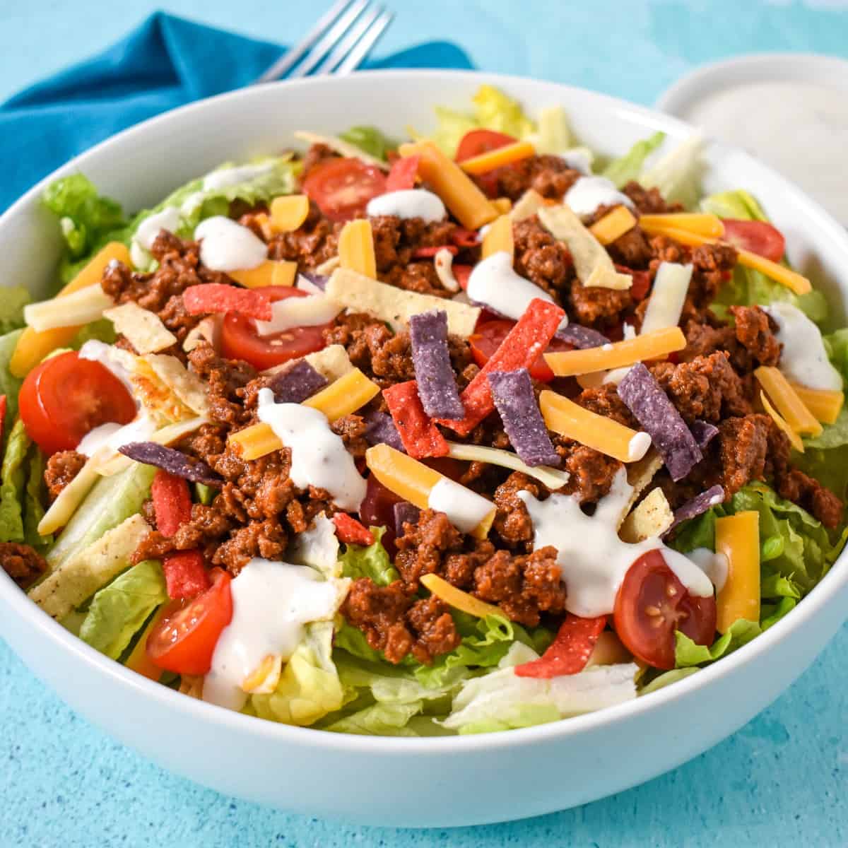 A close up of the salad served in a large white bowl and set on an aqua colored table.