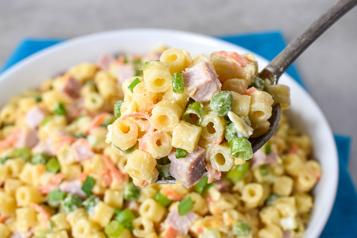 A spoonful of the finished pasta salad held over the white serving bowl.