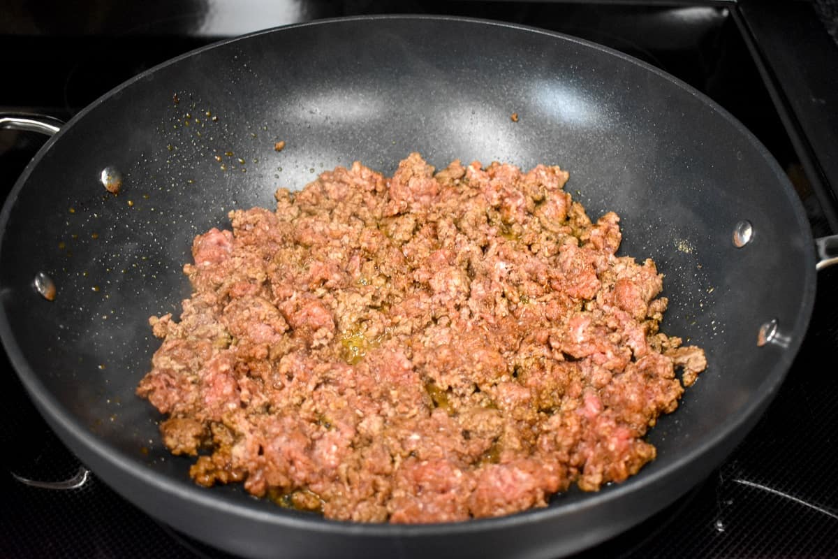 Seasoned ground beef cooking in a large, black skillet.